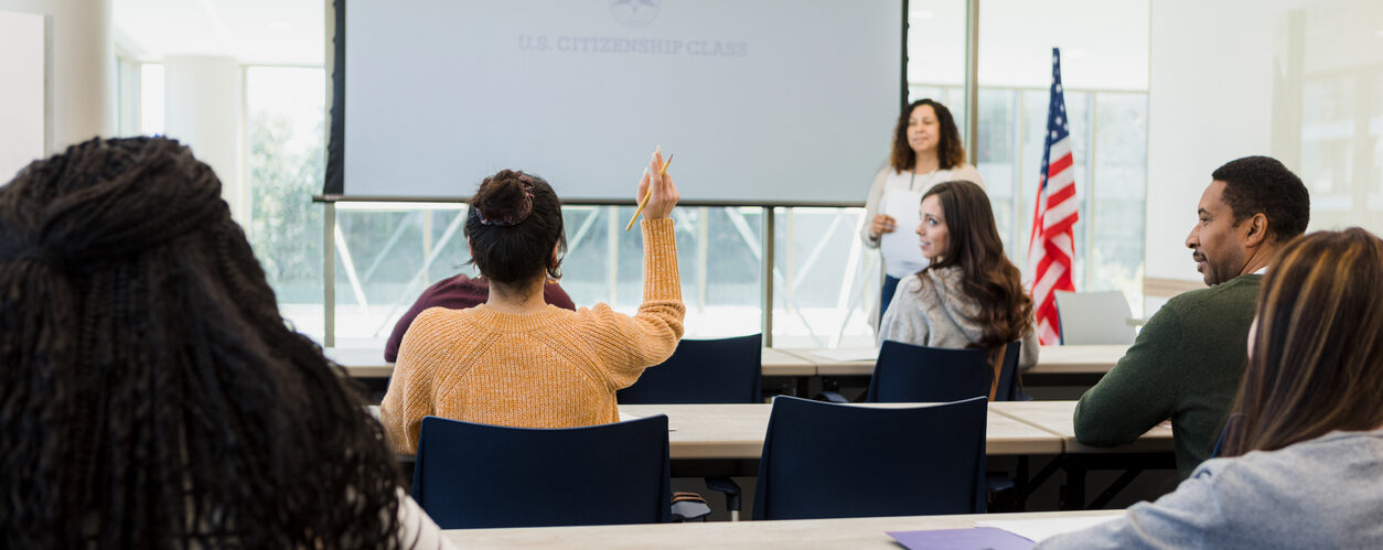 A rear view of a classroom full of diverse students taking an American citizenship class.